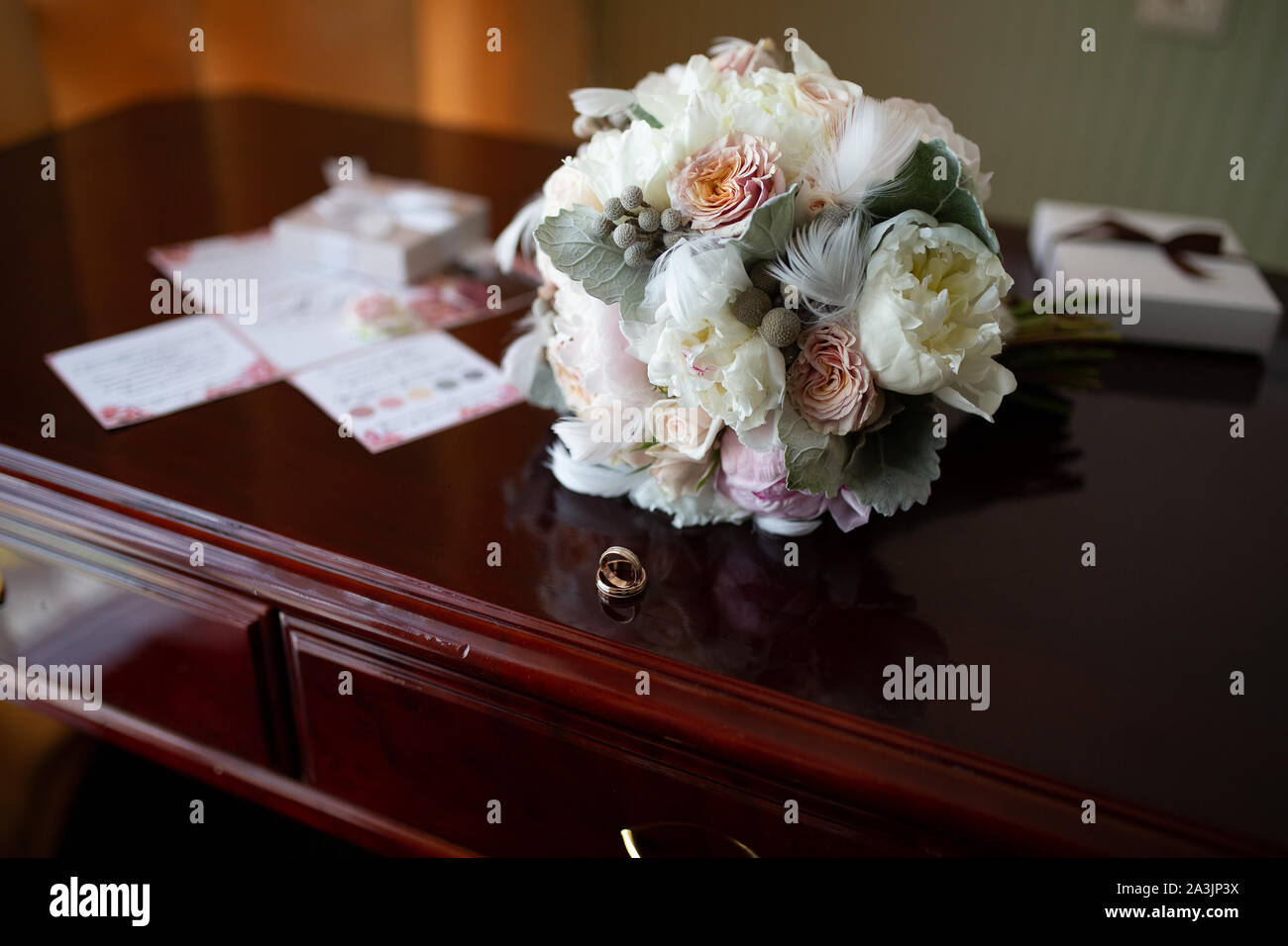 Wedding bouquet di peonie e rose giacente su un vintage in legno tavolo vicino gli anelli di nozze sullo sfondo del bando negli appartamenti di prepa Foto Stock