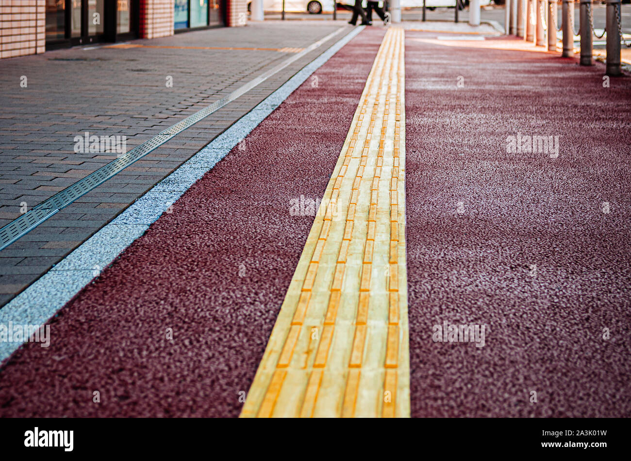 Guida di una tenda con pavimentazioni tattili, marciapiede marciapiede giallo guida per disabili e non vedenti. Messa a fuoco selettiva. Foto Stock