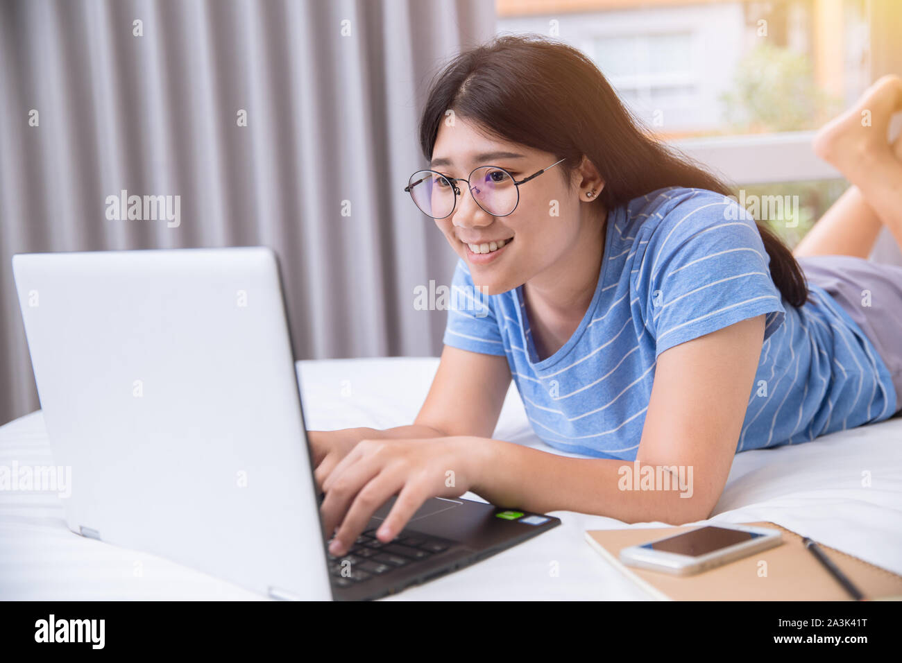 Girl Teen da stupidi sorriso lavorando compiti o chattare con gli amici tramite un pc portatile sul letto giorno del fine settimana. Foto Stock