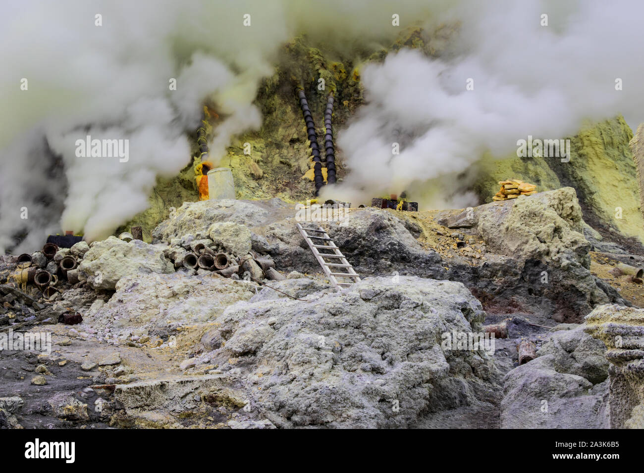 Miniere di zolfo il funzionamento in Mount Ijen cratere, Java Orientale, Indonesia. White i gas vulcanici passando da fessure nel terreno. Tubi in background. Foto Stock