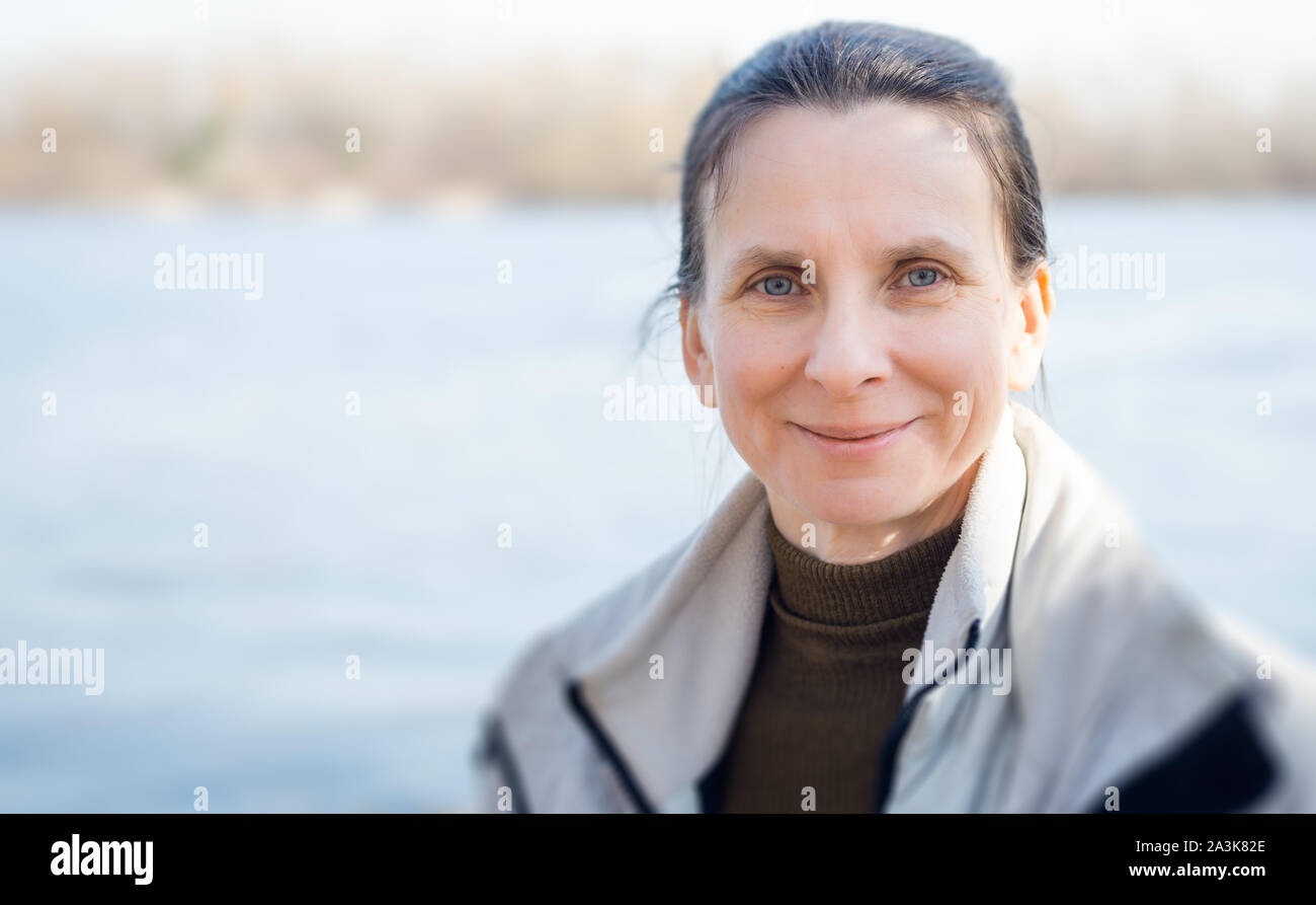 Un caldo e morbido ritratto di un bel sorriso positivo donna senior vicino al fiume, con copia spazio per il testo Foto Stock