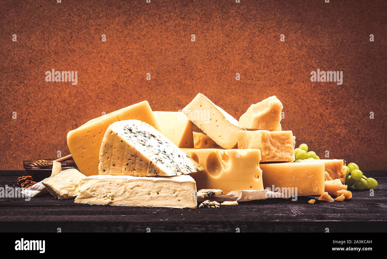 Diversi tipi di formaggio su tavoli in legno nero lo sfondo. Cumulo di cheddar, parmigiano, emmental, formaggi blu. Spazio copia foto, filtrato nel vintage sty Foto Stock