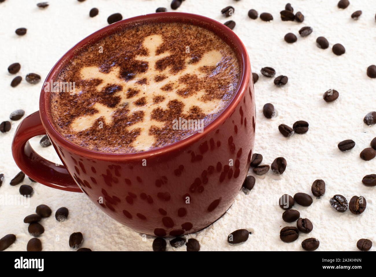 Un cappuccino con il simbolo del fiocco di neve al cioccolato motif, sfondo innevato e la dispersione di chicchi di caffè imposta la scena di una festa di Natale drink strappalacrime Foto Stock