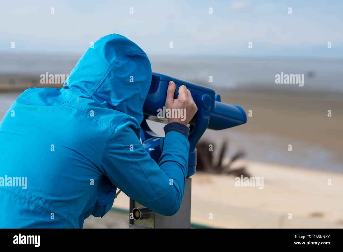 Uomo in blue coat cercando sul mare utilizzando gettone visione binoculare Foto Stock
