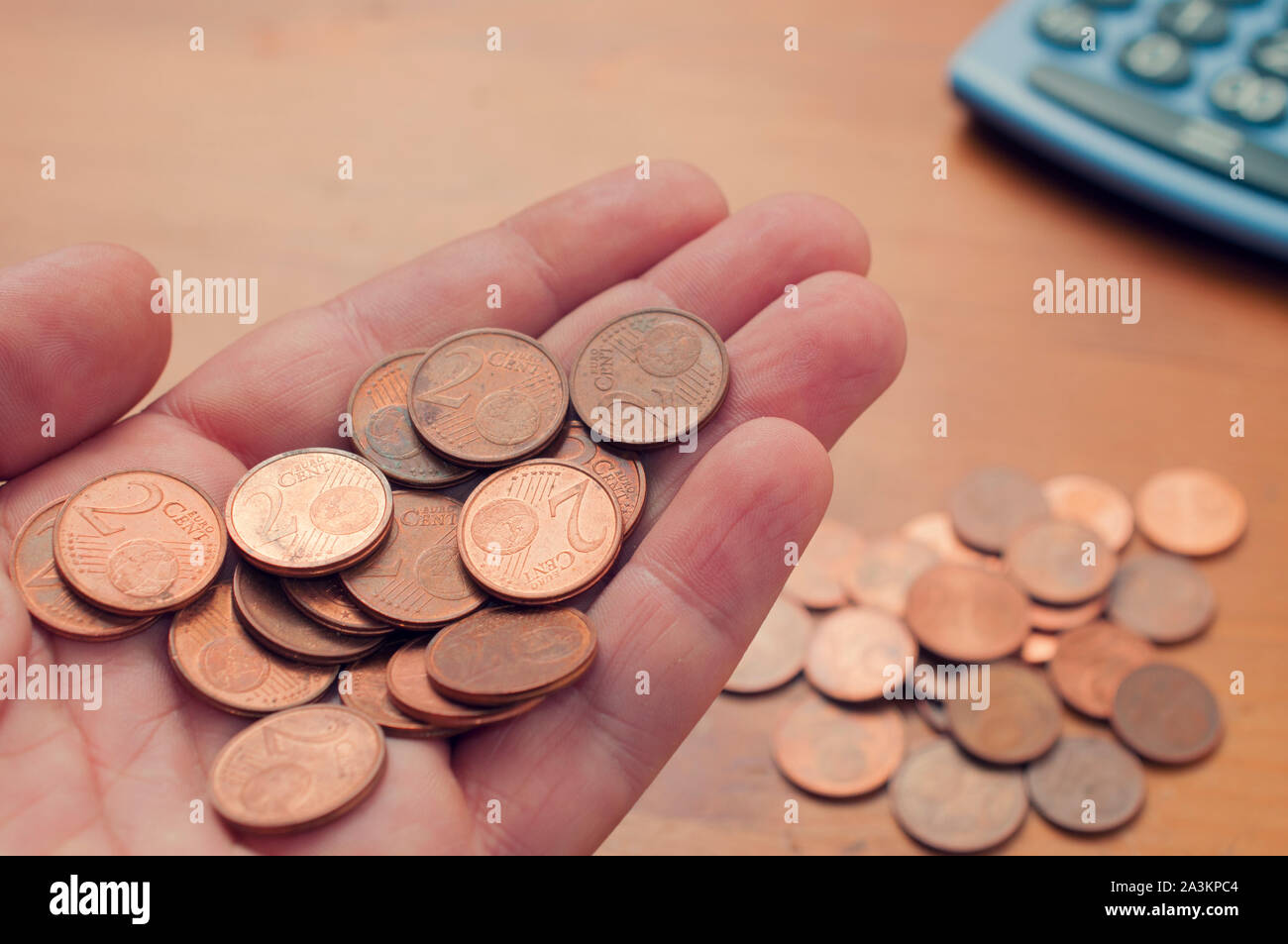 Man tenere una buch di due euro cent nel palmo della sua mano su una tabella con altre monete e di una calcolatrice Foto Stock