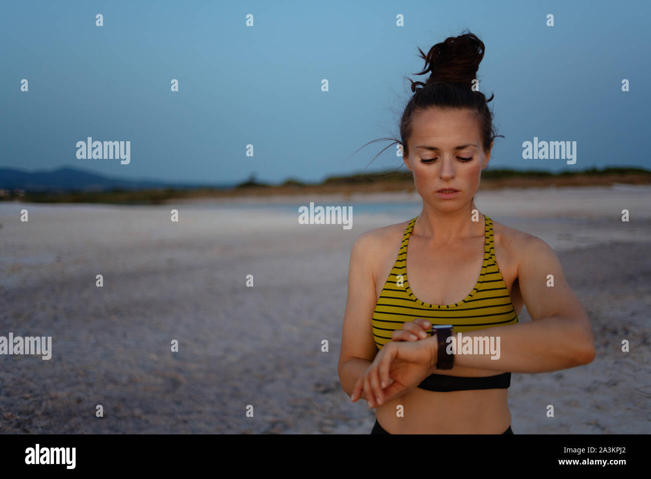 Sport fitness donna in stile sport vestiti sulla spiaggia la sera utilizzando smart guarda alla via peso in app fitness. Foto Stock