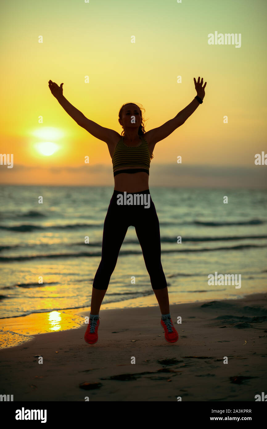 Silhouette di sport giovane donna in abiti da fitness in riva al mare in serata la formazione. Foto Stock