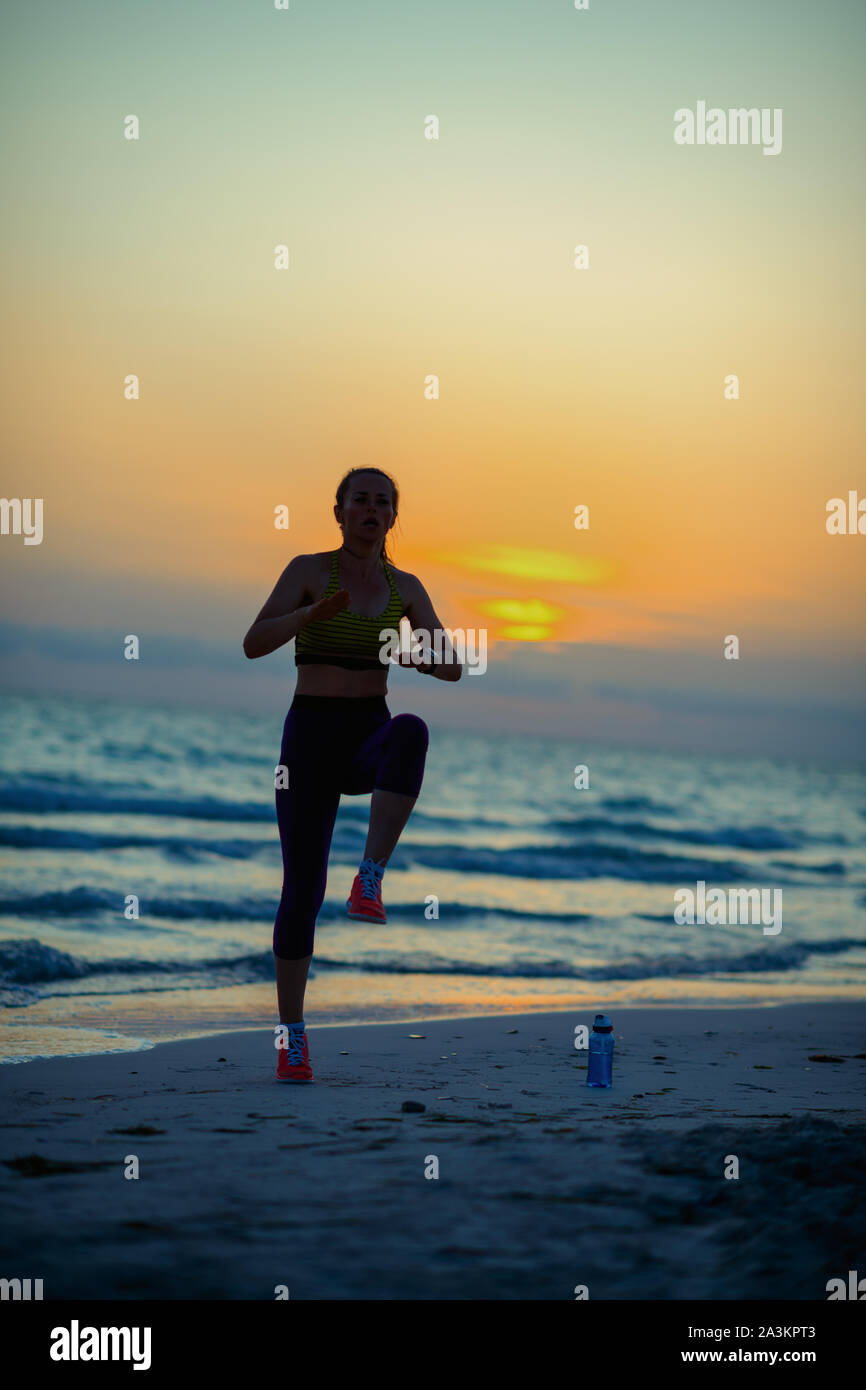 Silhouette di montare lo sport donna in abiti sportivi in riva al mare in serata la formazione. Foto Stock