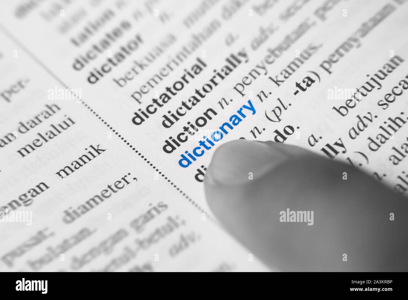 Close up di un dito puntato alla parola del dizionario in inglese a malay. dizionario traduttore e il concetto di linguaggio. Bianco e nero immagine monocromatica wit Foto Stock