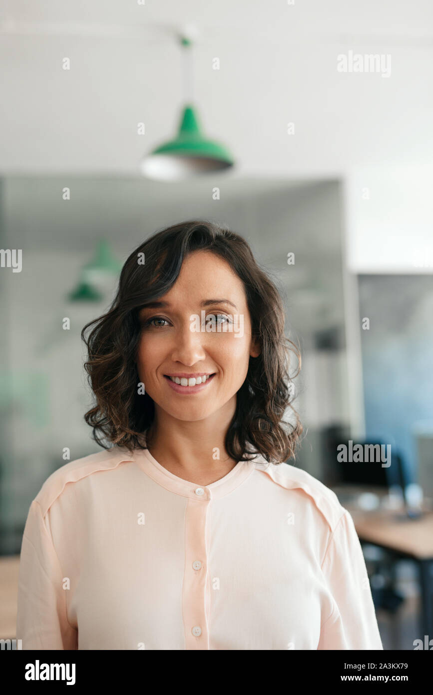 Sorridente giovane imprenditrice in piedi da se stessa in un ufficio moderno Foto Stock