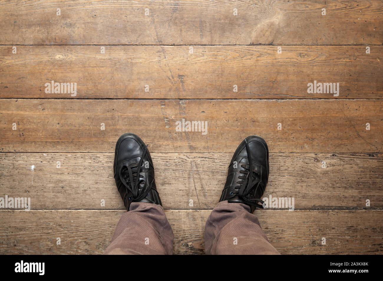 Piedini maschio in nero lucido scarpe in pelle stand su grungy pavimento in legno, la prospettiva in prima persona Foto Stock