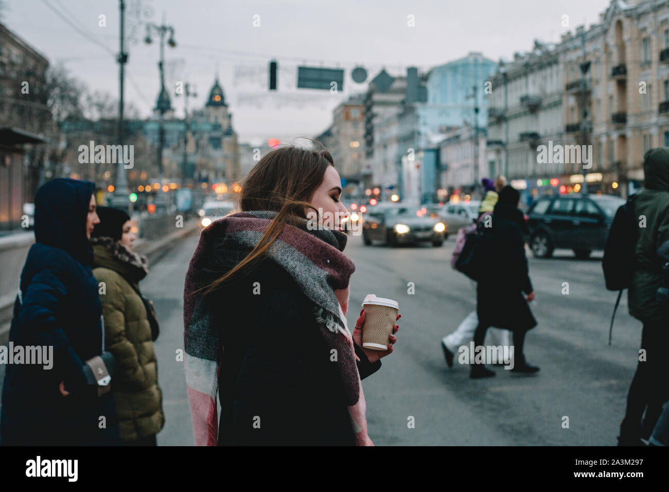 Donna con tazza monouso in abiti caldi attraversando una strada di città in inverno Foto Stock