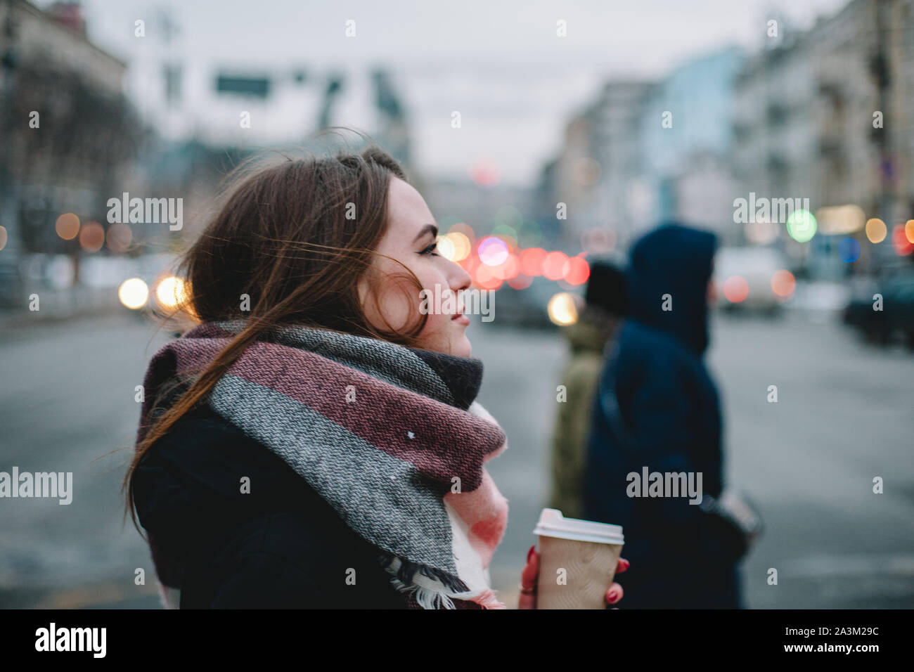 Donna con tazza monouso in abiti caldi attraversando una strada di città in inverno Foto Stock