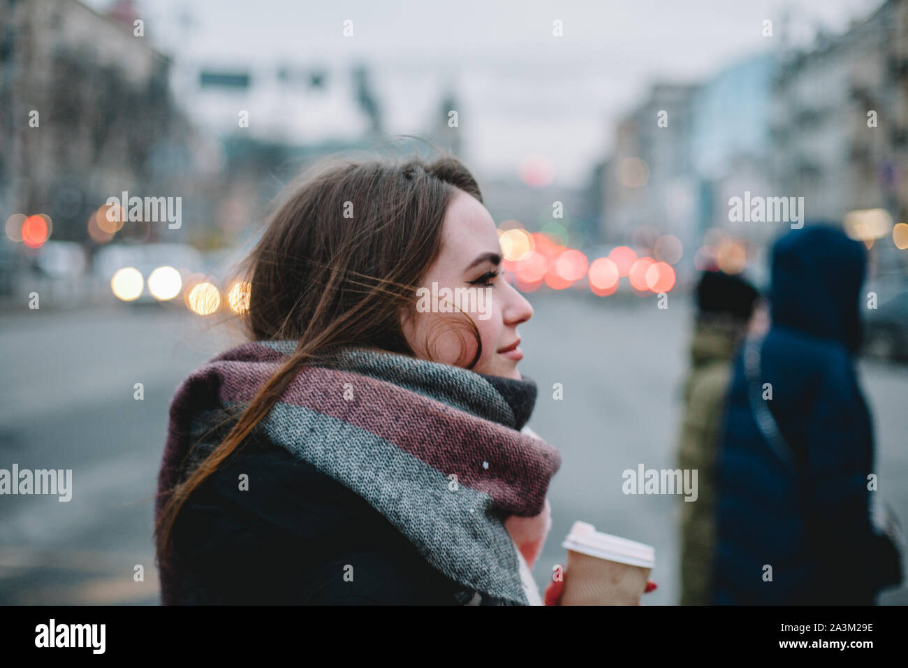 Donna con tazza monouso in abiti caldi attraversando una strada di città in inverno Foto Stock