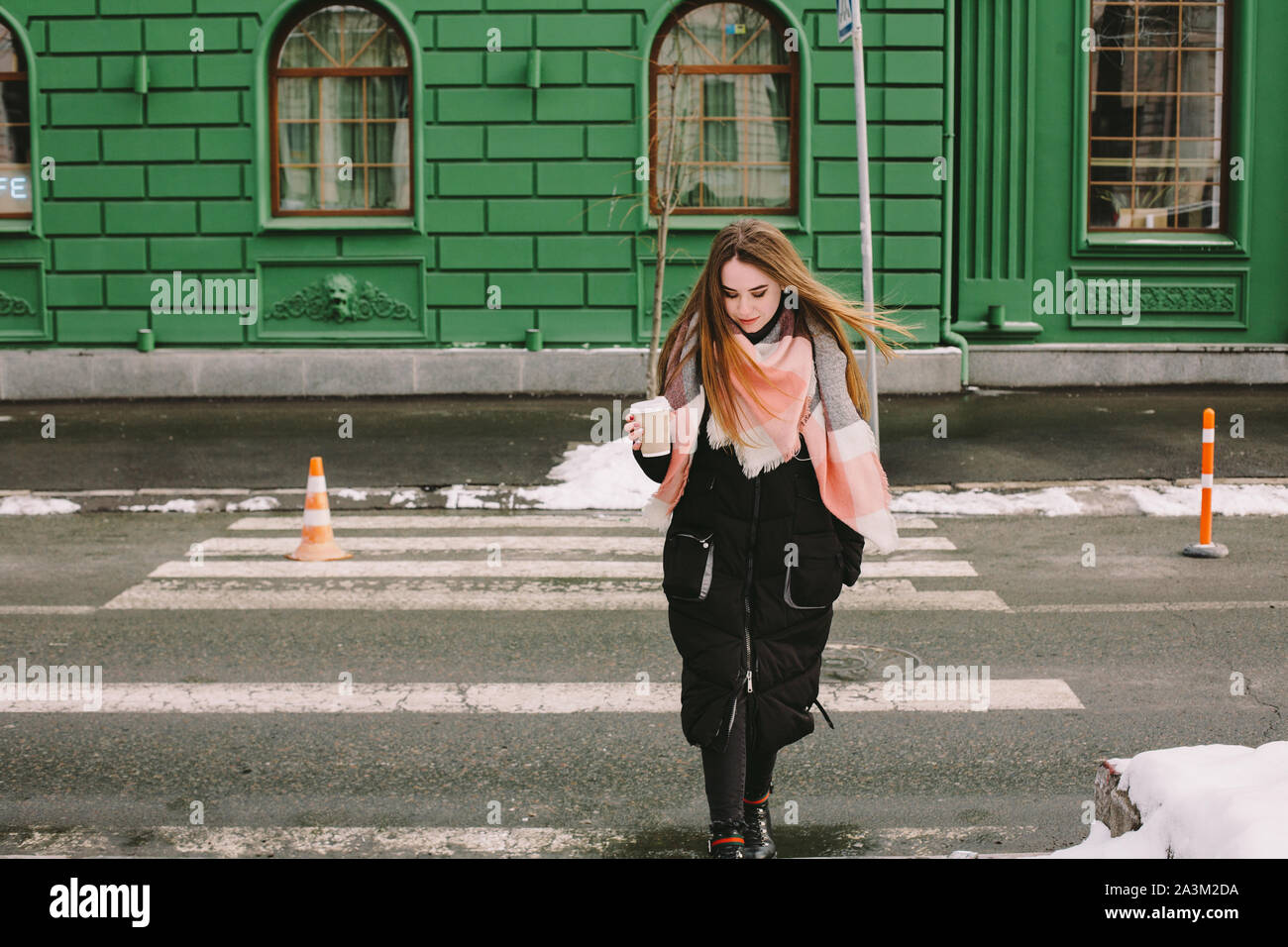 Considerato giovane donna in abiti caldi attraversando una strada di città in inverno Foto Stock