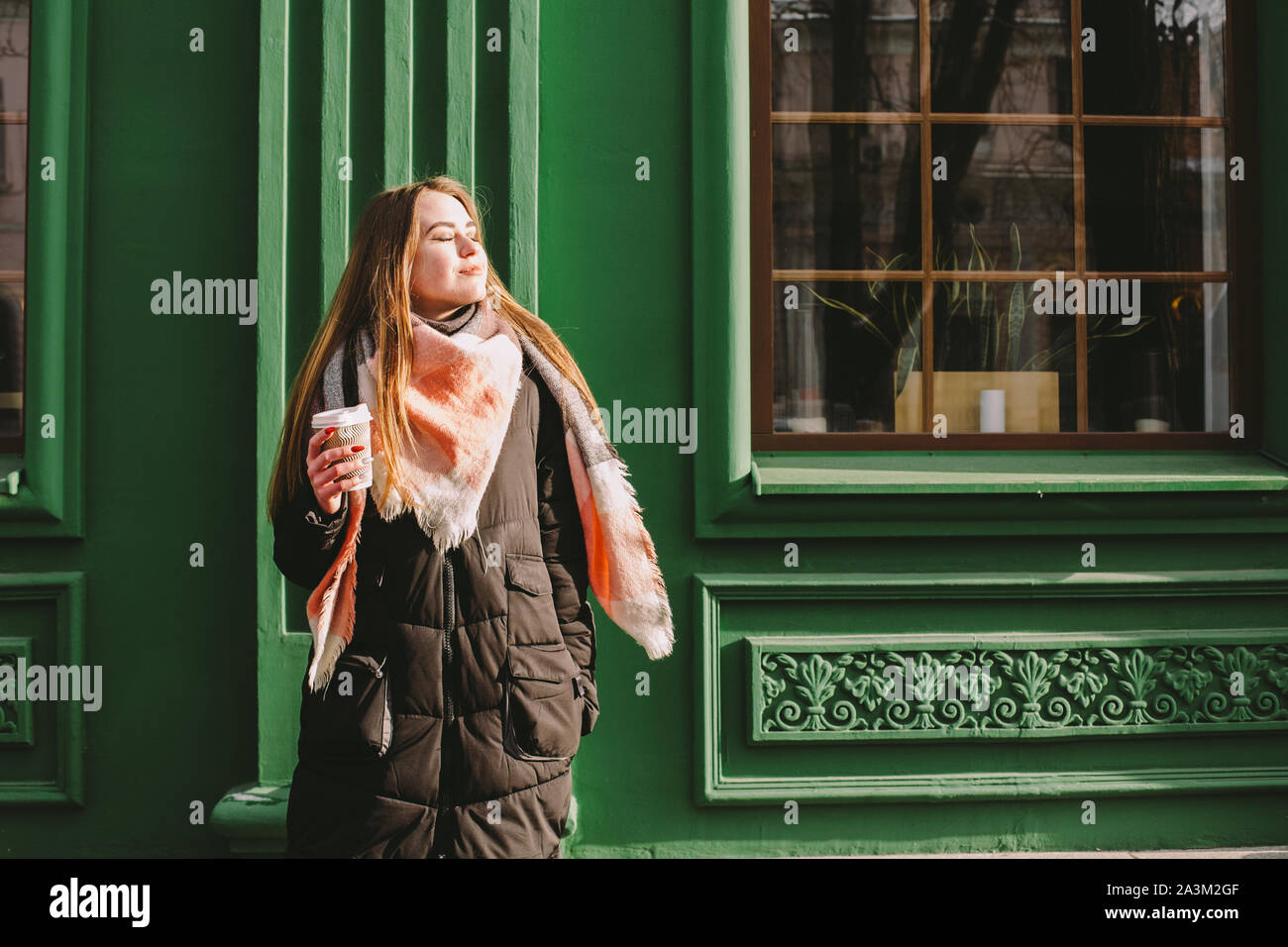 Triste donna in abiti caldi in piedi accanto al green building in via della città durante il periodo invernale Foto Stock