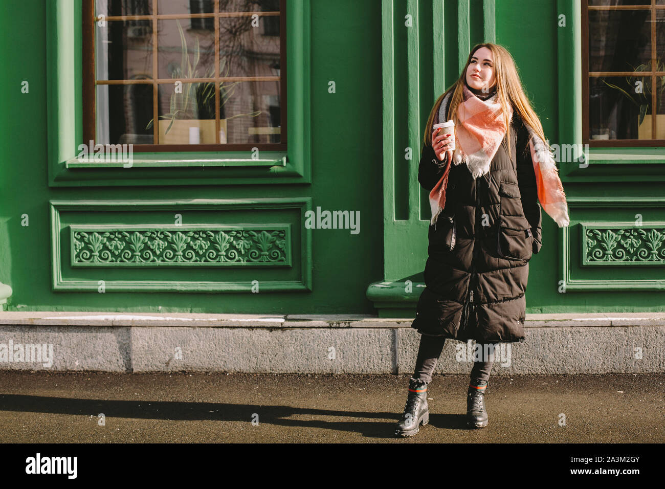Triste donna in abiti caldi in piedi accanto al green building in via della città durante il periodo invernale Foto Stock