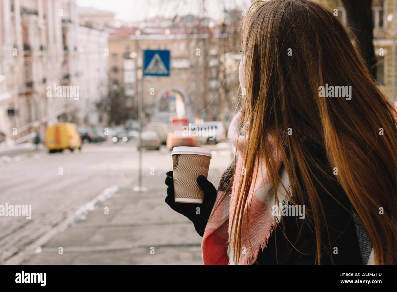 Donna con tazza monouso in abiti caldi in piedi in strada di città durante la stagione invernale Foto Stock