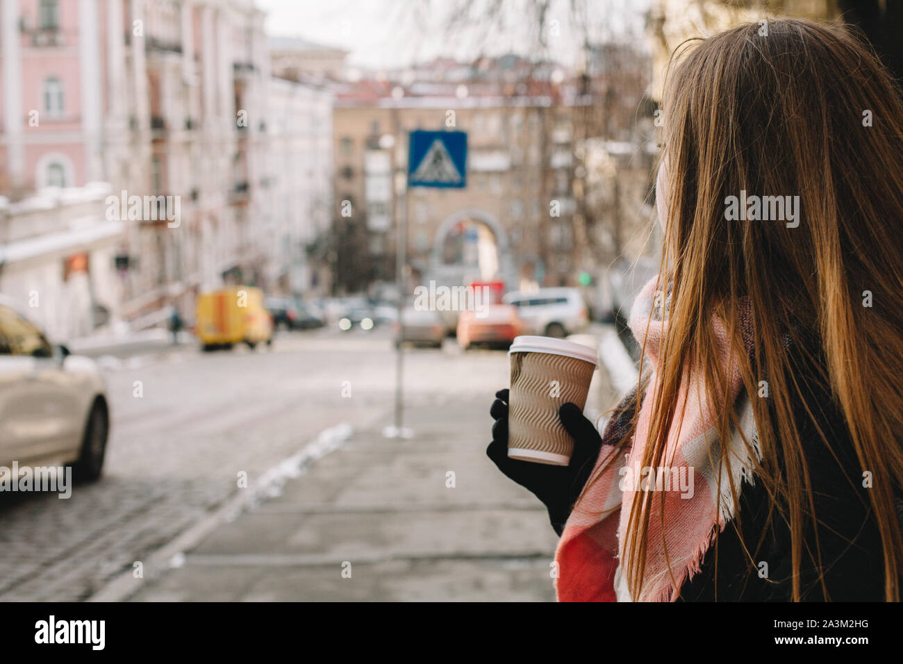 Donna con tazza monouso in abiti caldi in piedi in strada di città durante la stagione invernale Foto Stock