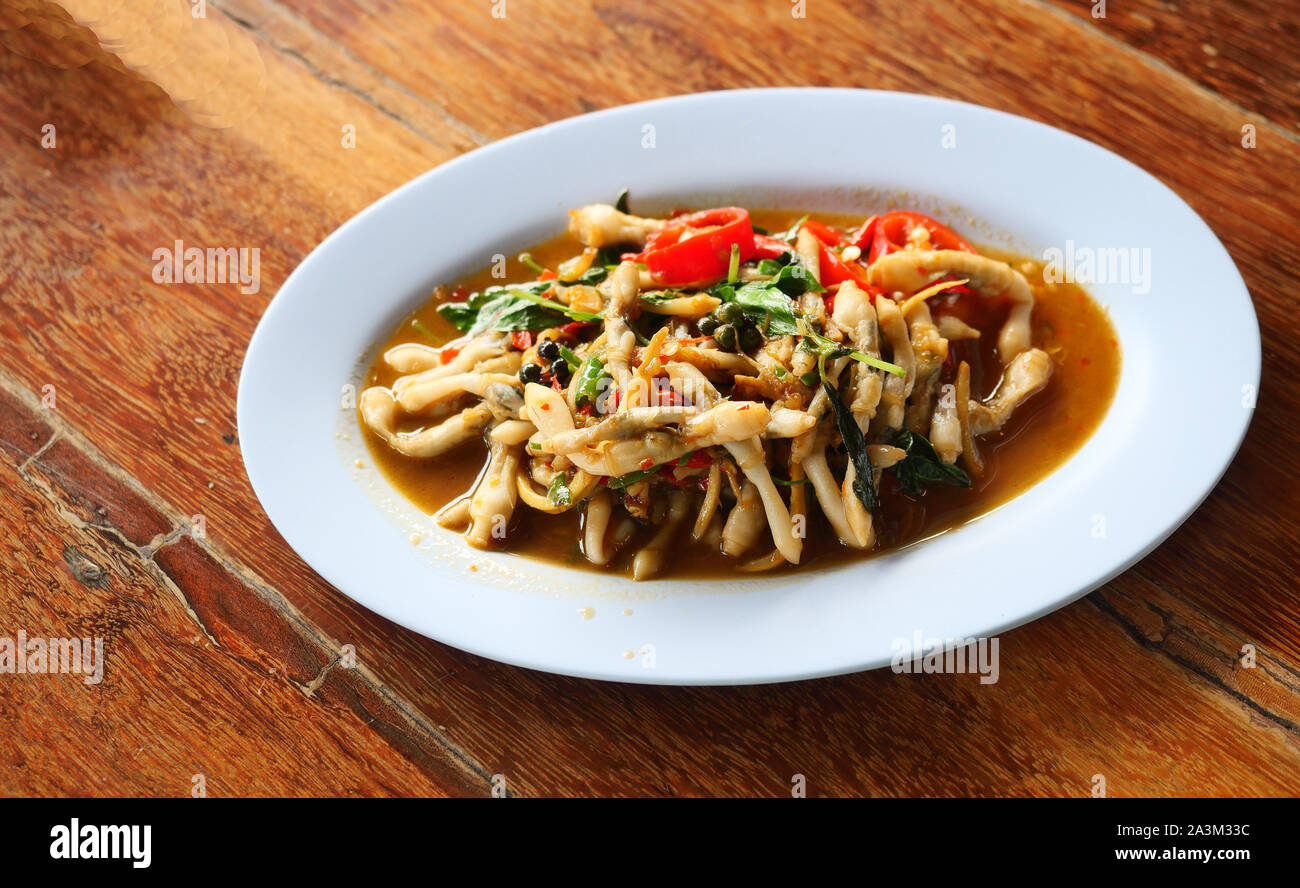 Fritti speziati stir cannolicchi con peperoncino e basilico, frutti di mare in un piatto bianco su marrone tavolo in legno tailandese, cucina locale in Thailandia Foto Stock