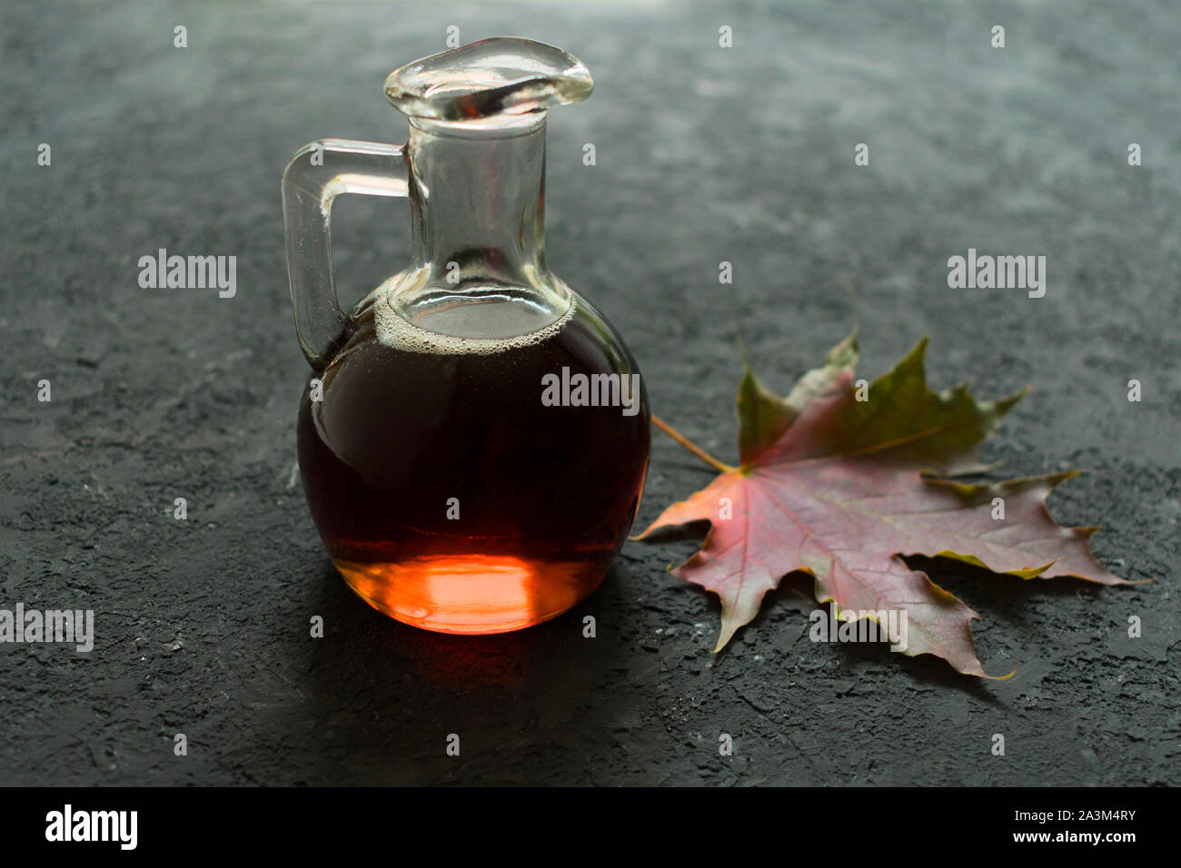 Bottiglia con sciroppo di acero e Foglia di acero su uno sfondo nero. Foto Stock