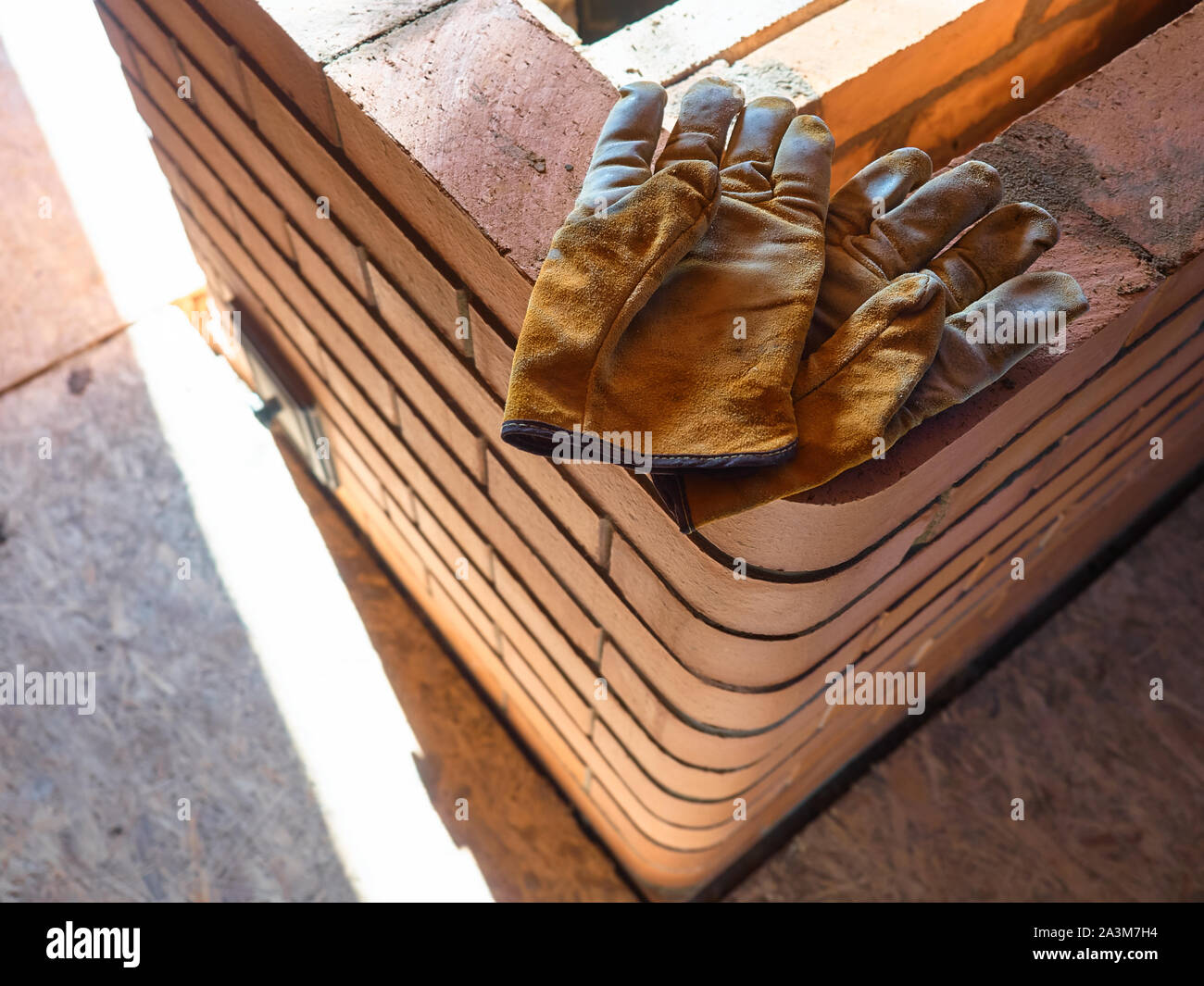 La stufa funzionante gauntlets giacciono sul bordo del rosso mattone di argilla stufa. Guanti da lavoro. Foto Stock