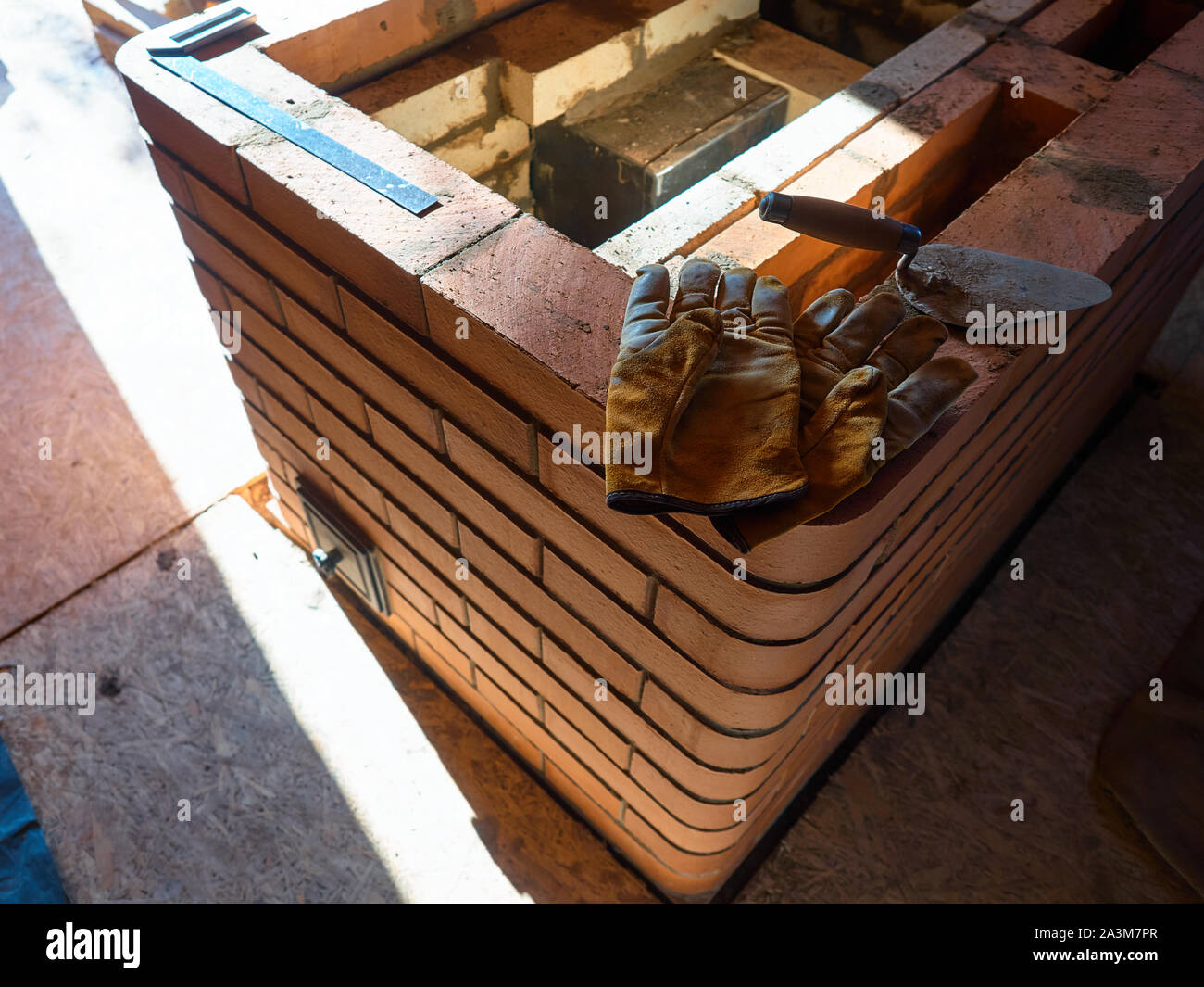 La stufa funzionante gauntlets giacciono sul bordo del rosso mattone di argilla stufa. Guanti da lavoro. Foto Stock