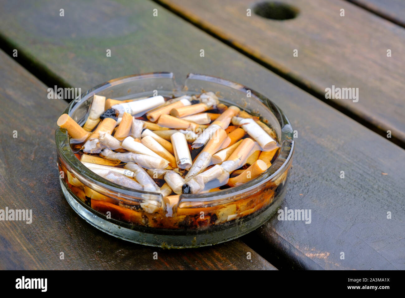 Posacenere pieno di mozziconi di sigarette su una tabella dopo la pioggia Foto Stock