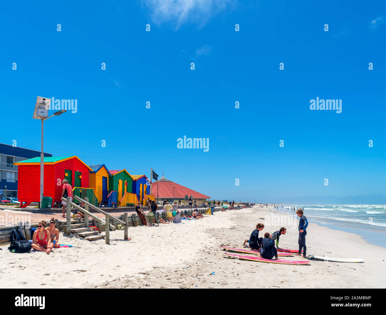 Surfers di fronte colorata spiaggia vittoriano capanne in Muizenberg, Cape Town, Western Cape, Sud Africa Foto Stock
