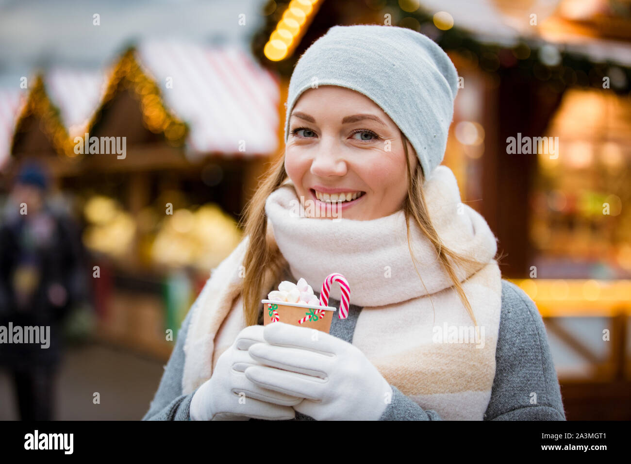 Giovane donna nel mercato di Natale di bere tazza di cioccolata calda con  marshmallow maglia da indossare caldo cappello e sciarpa. Illuminata e  decorata negozi Foto stock - Alamy