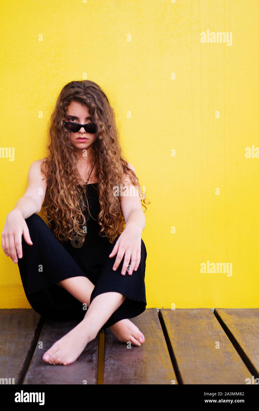 Cool ragazza adolescente indossando occhiali da sole contro sfondo giallo Foto Stock