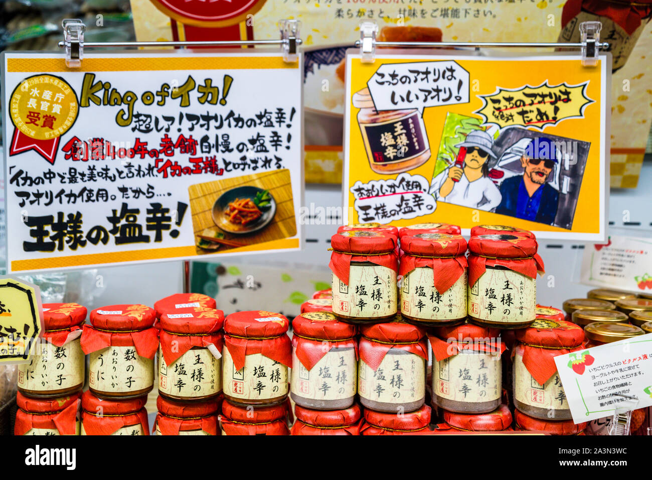 Un cartello pubblicitario promuove “Re di Ika!” – shiokara di calamari fermentati a partire da calamari aori secondo una ricetta tramandata da 400 anni da un produttore radicato da tempo, al Museo Izu Wasabi, Kannami, Prefettura di Shizuoka, Giappone. Vasetti con tappo rosso della specialità sono in vendita. Foto Stock
