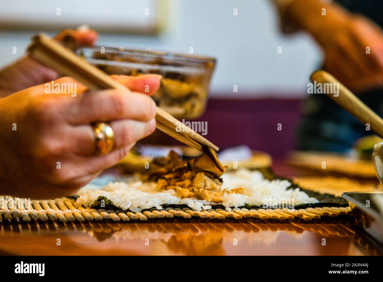 Una mano usa le bacchette per sovrapporre riso e pesce affettato sottilmente su una foglia di nori – preparazione per il sushi futomaki nel workshop di bento di Kayoko Kawamura, Izunokuni, penisola di Izu, Giappone. Foto Stock