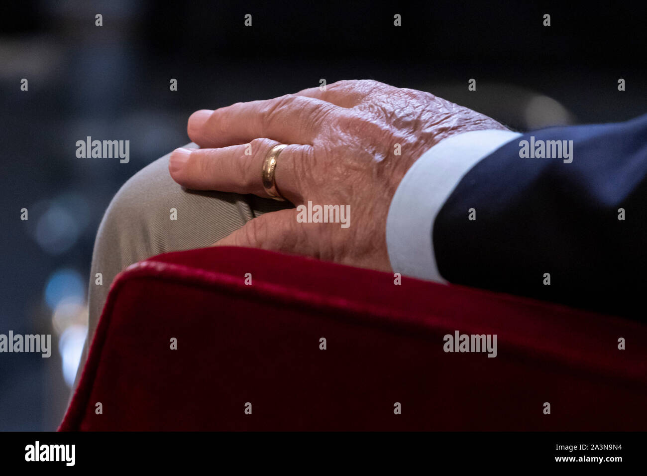 Mano dell'uomo a riposo sul ginocchio, con anello/fascia di nozze d'oro sul dito dell'anello. Foto Stock