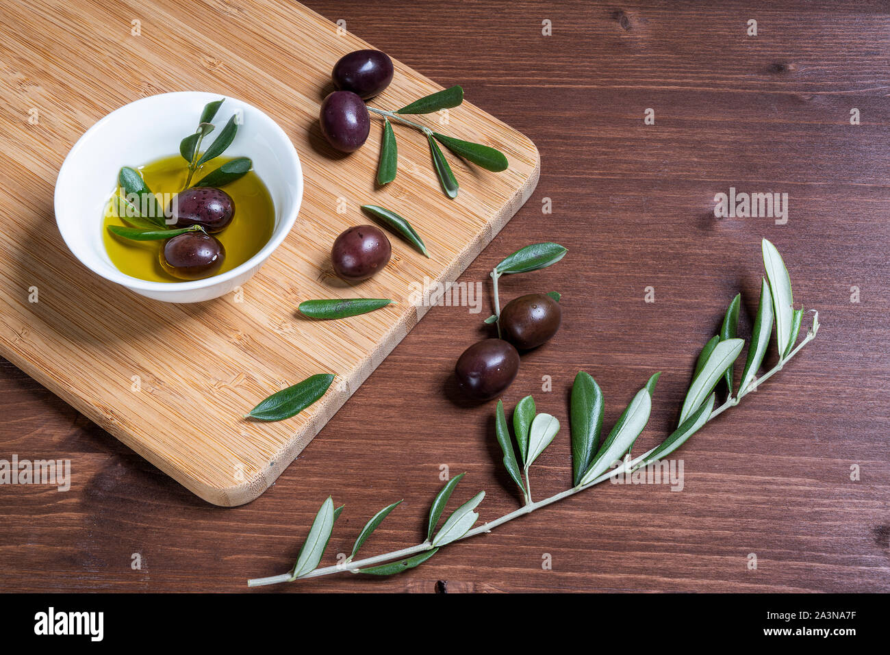 Olio di oliva e di olive su una piastra su una superficie di legno con alcuni rami di olivo Foto Stock