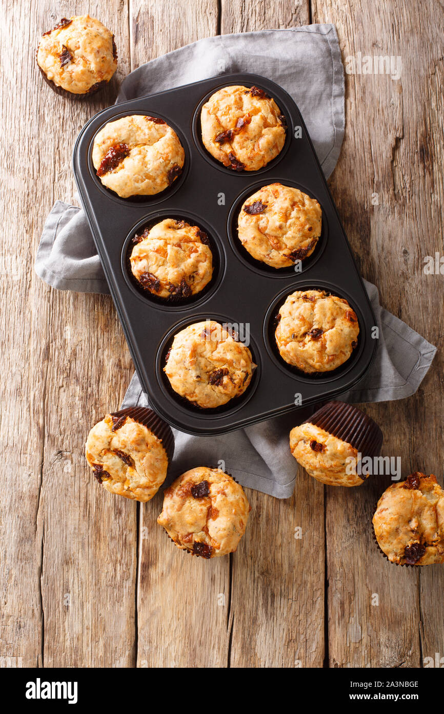 Muffin alla mediterranea con pomodori secchi e formaggio cheddar close-up in una teglia sul tavolo. Verticale in alto vista da sopra Foto Stock