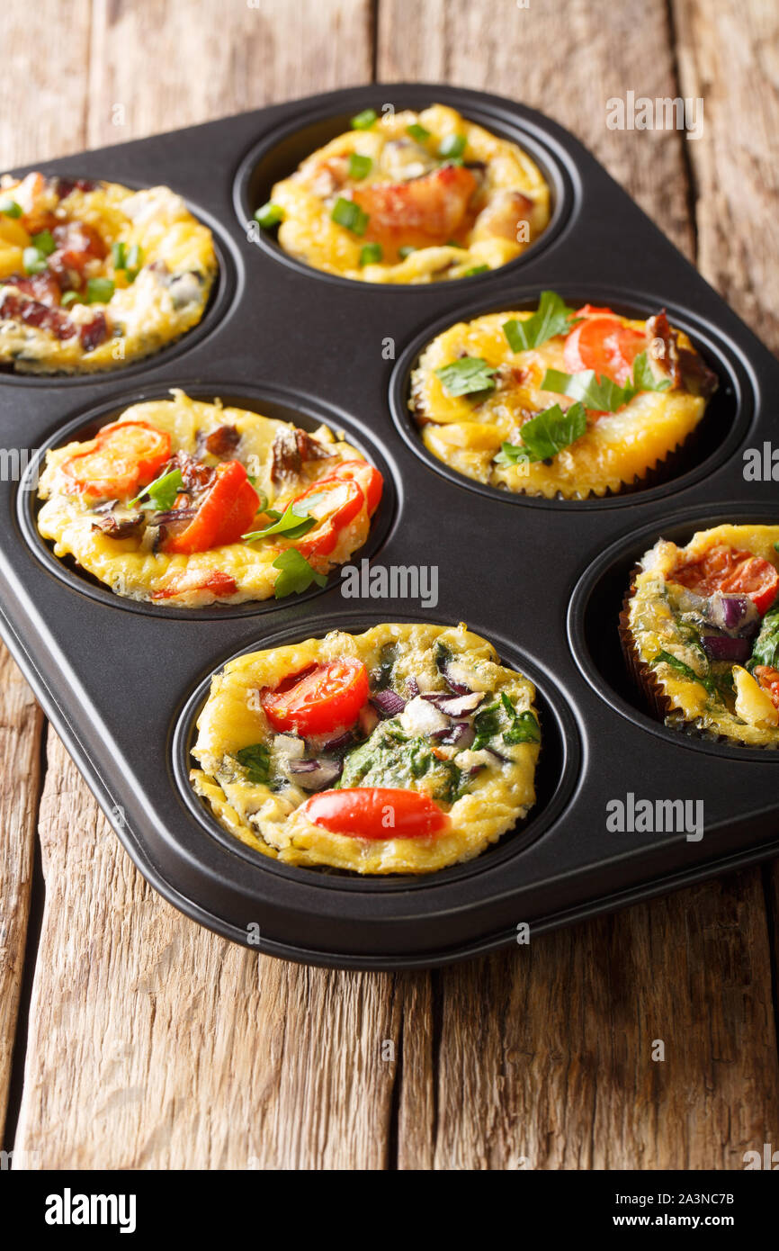 Uovo muffin frittata con pancetta, pomodori, spinaci e funghi close-up in una teglia sul piano verticale. Foto Stock