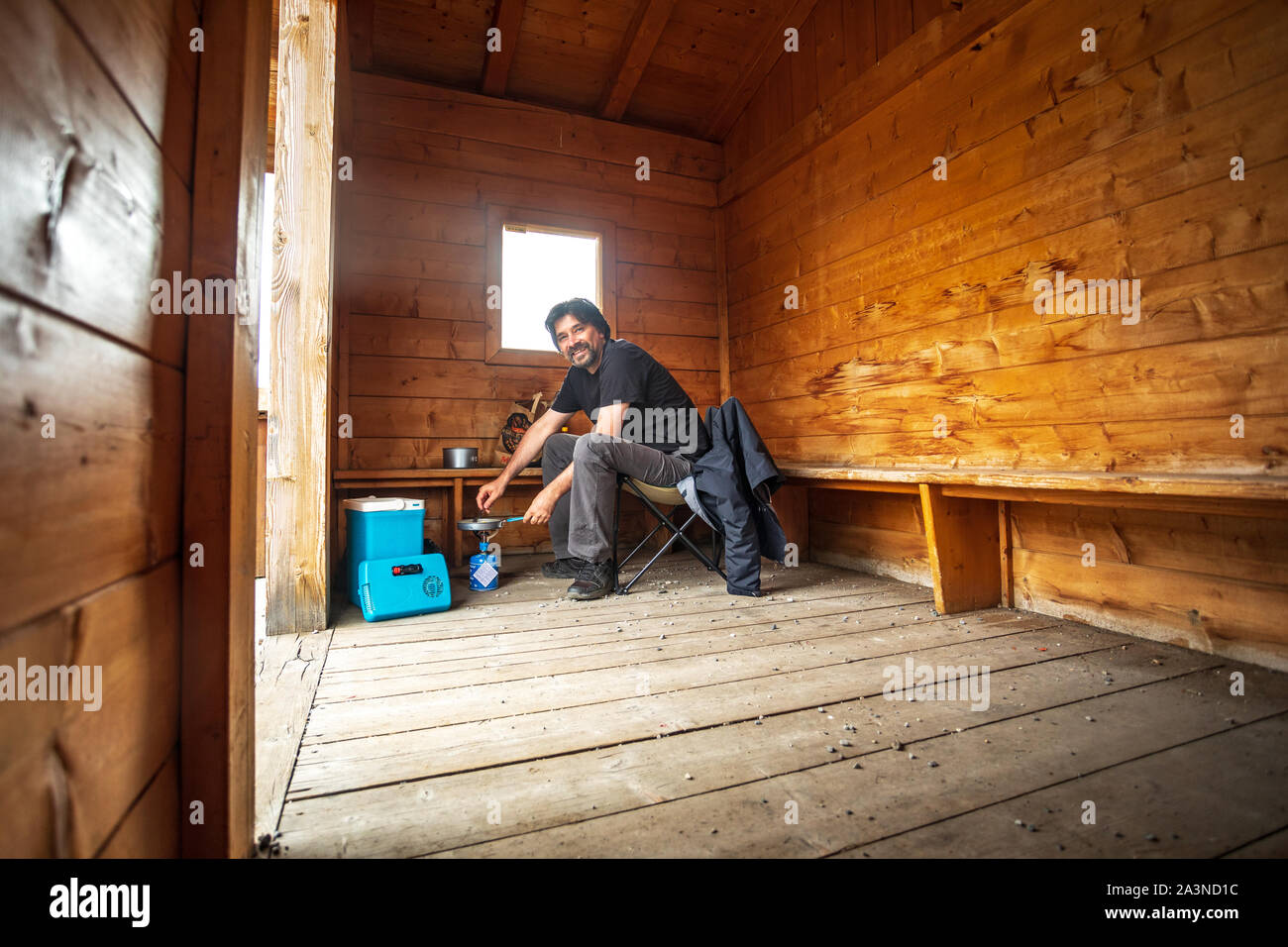 Uomo che cucina cibo sul gas campeggio in una cabina di legno Foto Stock