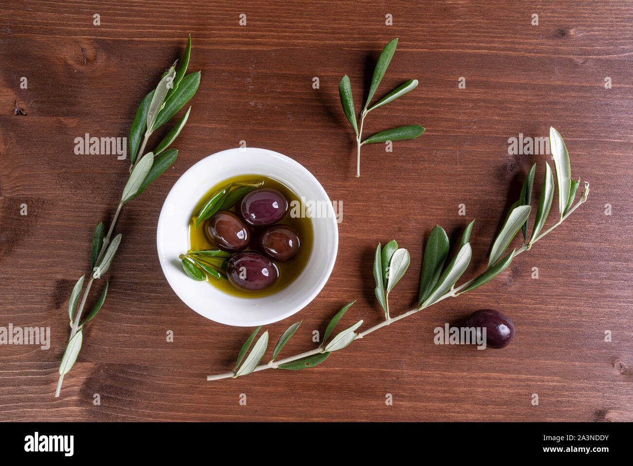 Olio di oliva e di olive su una superficie in legno con alcuni rami di olivo Foto Stock