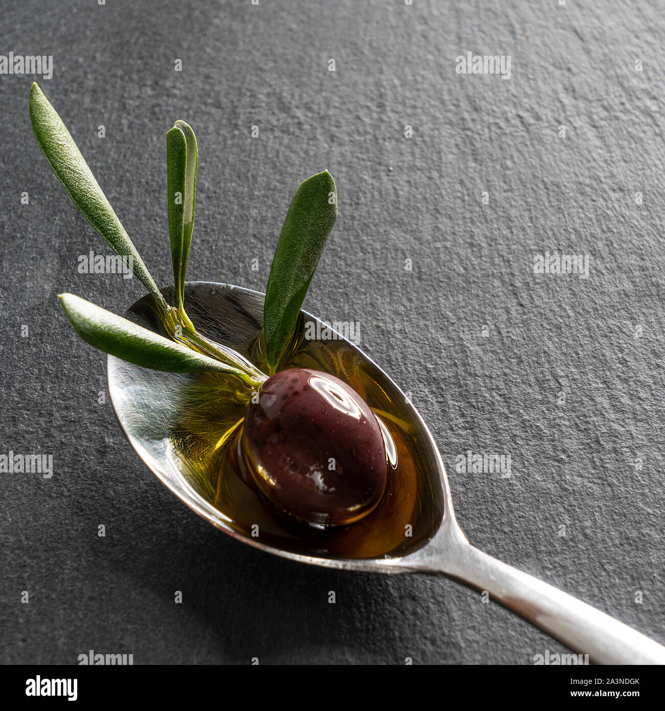 Una oliva nera nel cucchiaio con una pietra nera Foto Stock