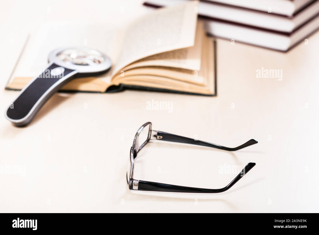 Libro di lettura con low vision - occhiali con lente di ingrandimento sul libro aperto vicino a pila di libri sulla tabella pallido (messa a fuoco in primo piano) Foto Stock