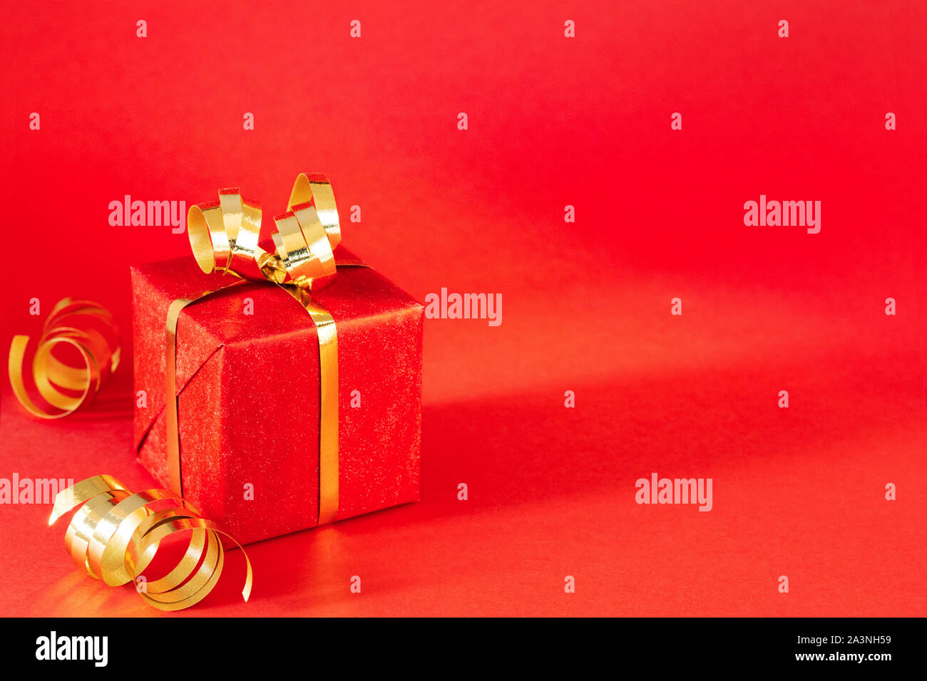 Confezione regalo rossa con golden bow e streamers su sfondo rosso. In stile minimale natale e concetto di compleanno. Girato l'angolo. Foto Stock