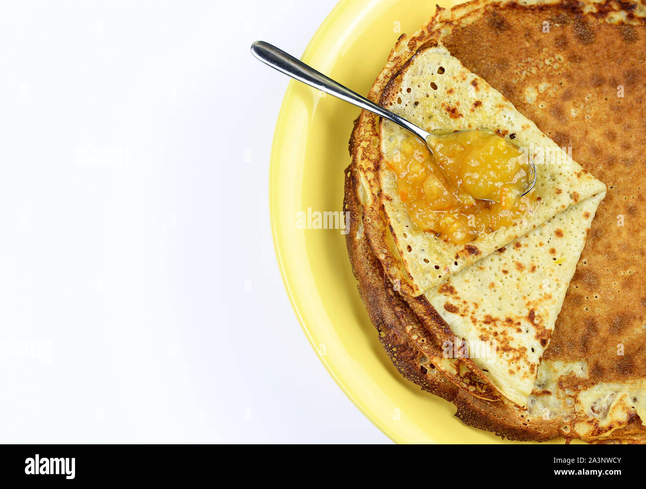 Crepes piegato in quattro sulla piastra di colore giallo e marmellata di arance amare con cucchiaio su sfondo bianco. Vista superiore Foto Stock