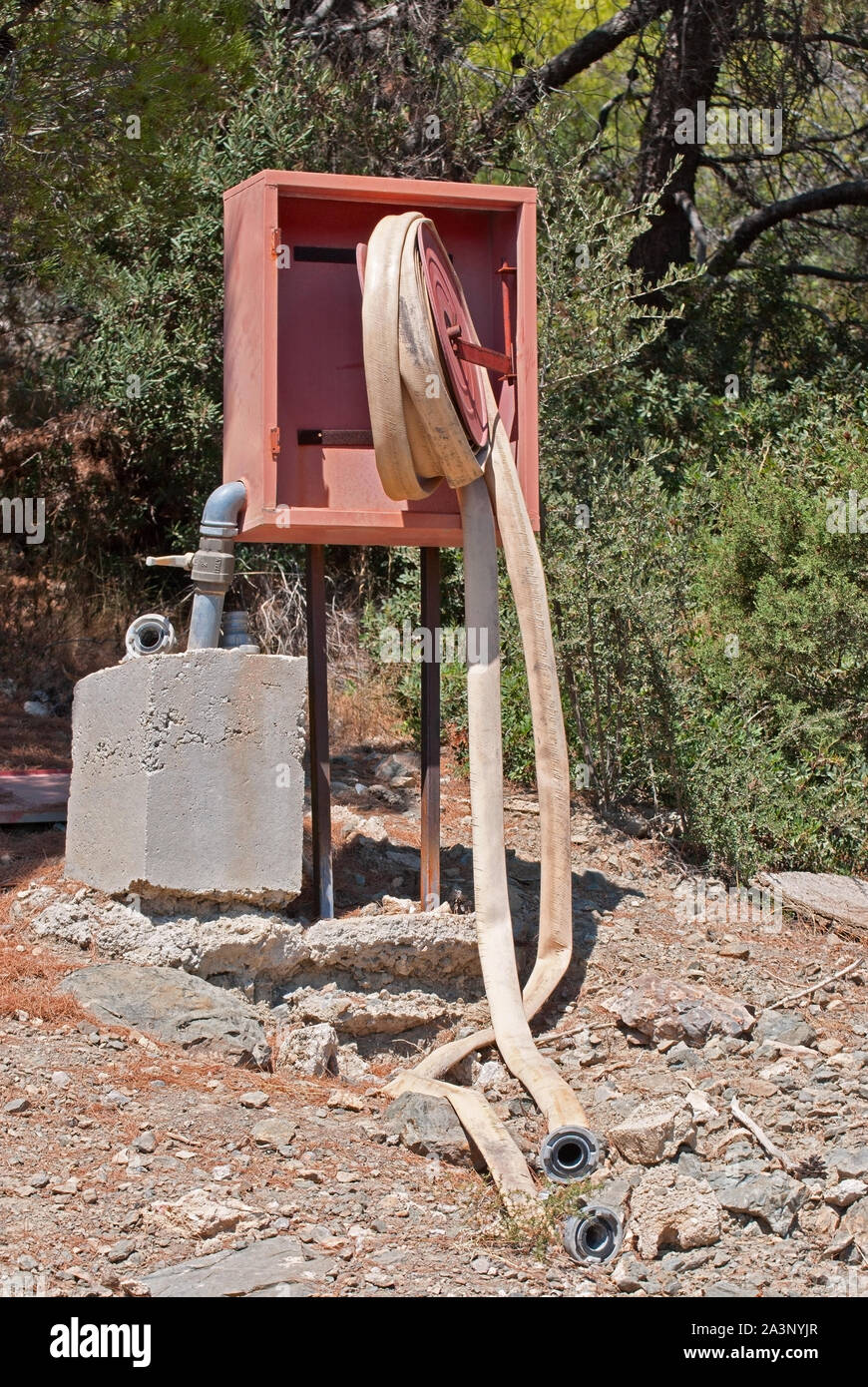 Abbandonato red fire shield non ritorti con tubo antincendio in piedi nella foresta sul versante di una montagna. La città di Anavissos, Grecia. Foto Stock