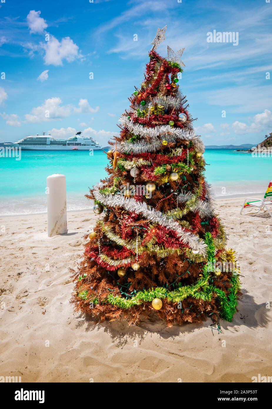 Albero di Natale decorato sulla sabbia bianca della spiaggia caraibica, Jost Van Dyke, Isole Vergini Britanniche. La nave di crociera in background. Foto Stock
