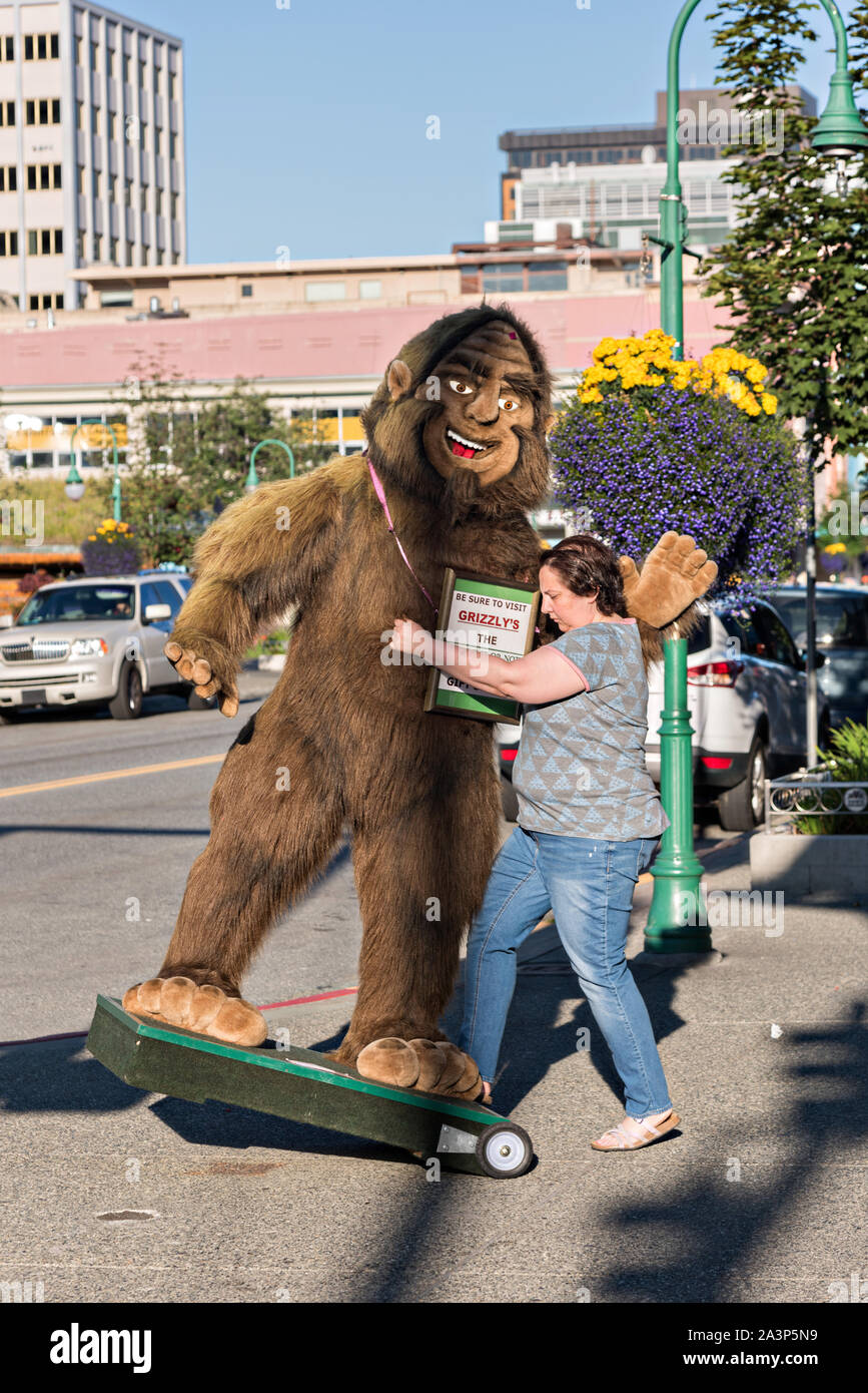 Un lavoratore si trasferisce un gigante farcita Bigfoot o Sasquatch presso un negozio lungo la quarta Avenue nel centro cittadino di Anchorage in Alaska,. Foto Stock