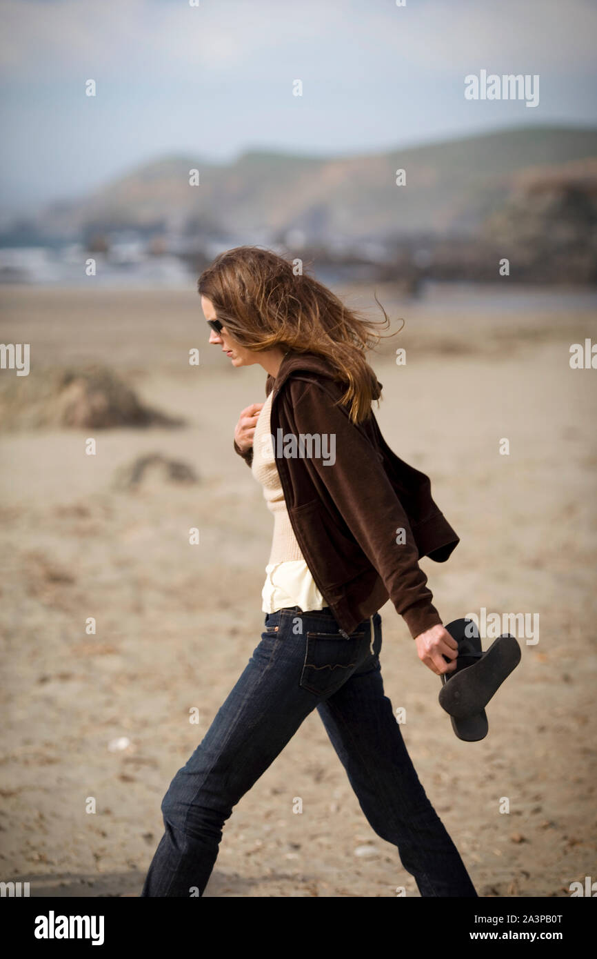 Giovane donna che porta le sue scarpe mentre si cammina su una spiaggia. Foto Stock