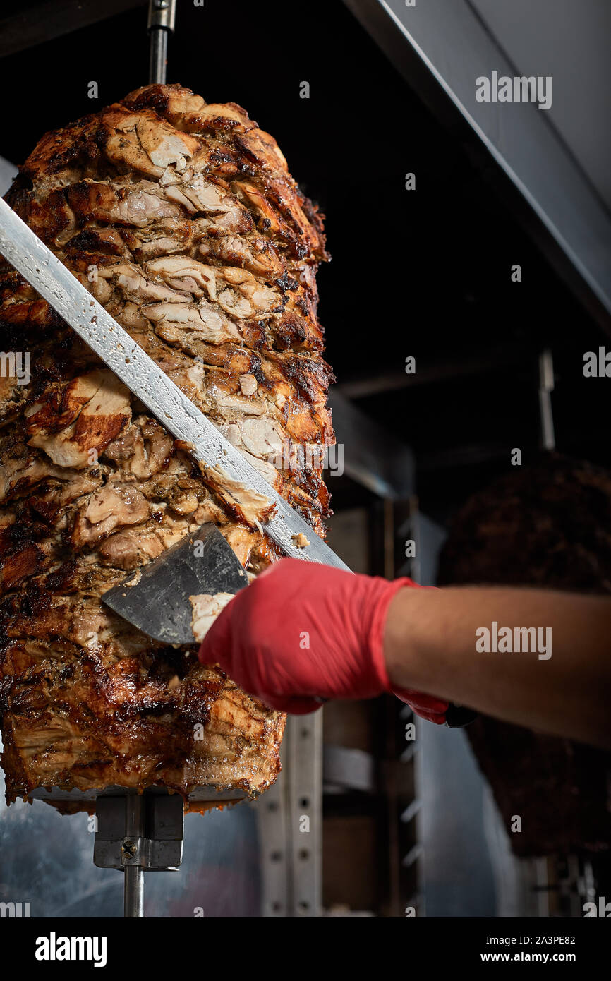 Arrosto di carne con osso per la preparazione di donatori o shawarma. Close-up. Il cuoco taglia la carne fritta su carbone per la preparazione di shawar Foto Stock