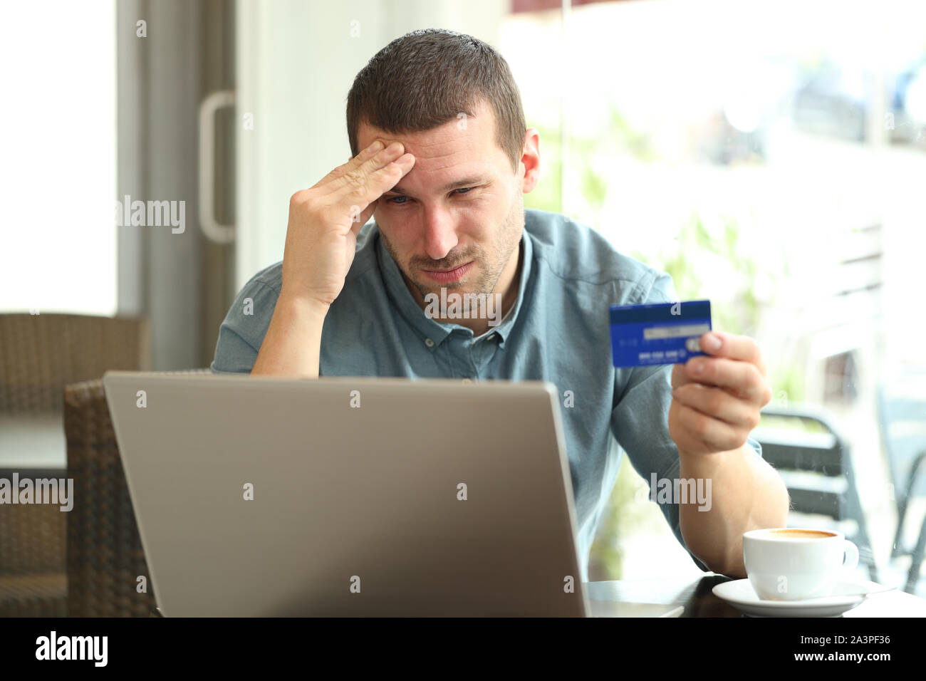 Frustrato uomo pagando con carta di credito e il computer portatile seduti in un caffè Foto Stock