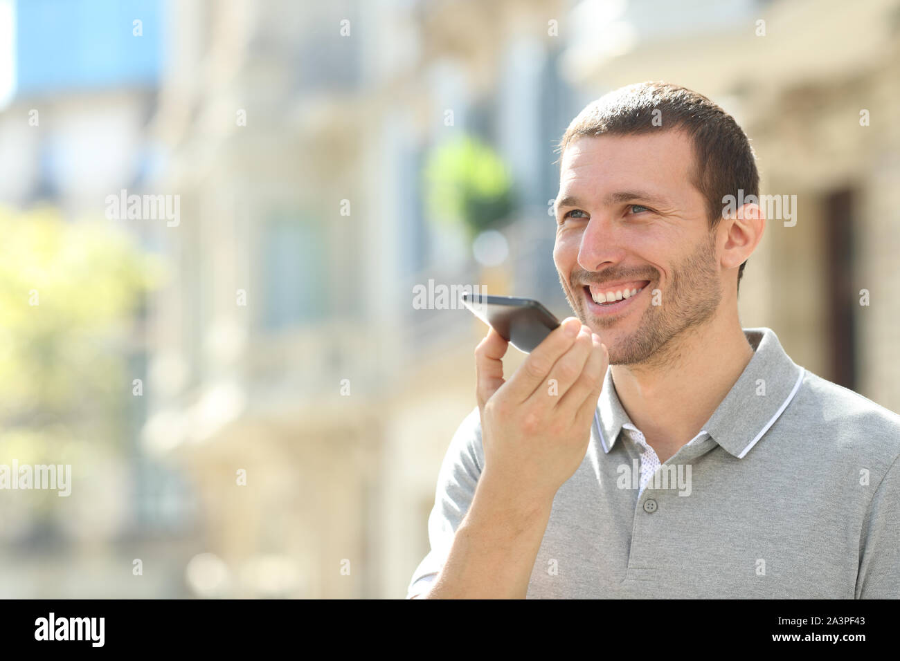 Felice l'uomo utilizza il riconoscimento vocale sul telefono cellulare per inviare un messaggio registrato in strada Foto Stock